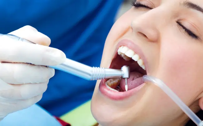 Patient receiving root canal treatment in Muscat while a dentist uses a dental handpiece and suction instrument during an endodontic procedure.